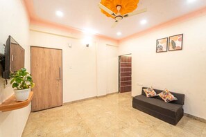 A room with a ceiling fan, a sofa with patterned cushions, a potted plant, and a wooden door.