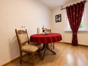 Ein Esszimmer mit einem runden Tisch, zwei Stühlen, einer Vase mit Blumen und einem Fenster mit Vorhängen.