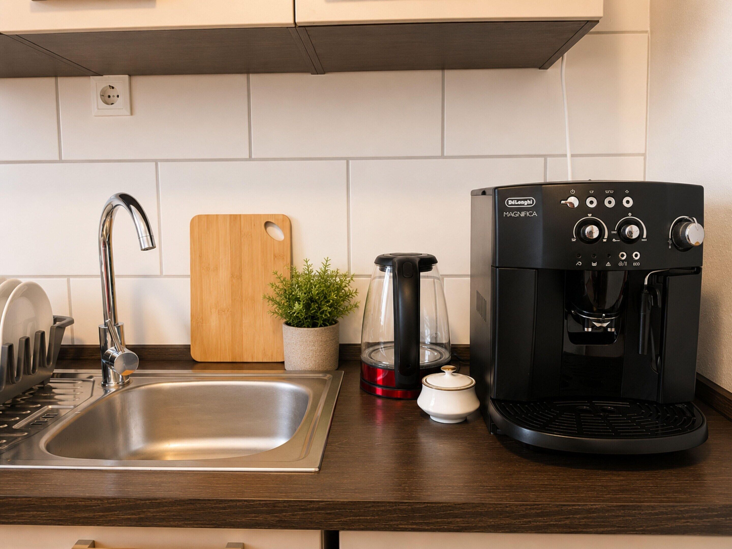 Una cocina con un lavamanos de acero inoxidable, una tabla de cortar de madera, una cafetera y una planta en maceta.