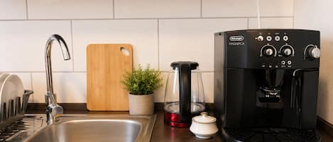Una cocina con un lavamanos de acero inoxidable, una tabla de cortar de madera, una cafetera y una planta en maceta.