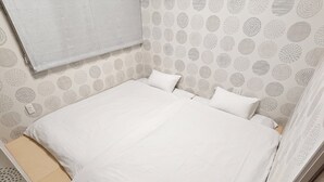 A neatly made bed with a white bedspread and pillows, a wall with a circular pattern, and a small window with a white blind. - SA INN (Taito City)