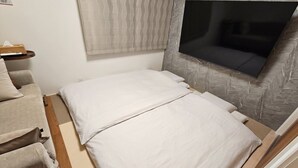 A compact room with a bed, a small seating area, and a television mounted on the wall. - SA INN (Taito City)