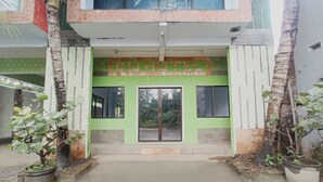 Entrada de un hotel con fachada verde, un cartel y un acceso con portones.