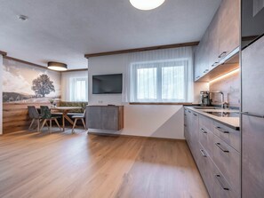 Ett modernt kök med en inbyggd ugn, en matplats med bord och stolar samt ett stort fönster med gardiner.