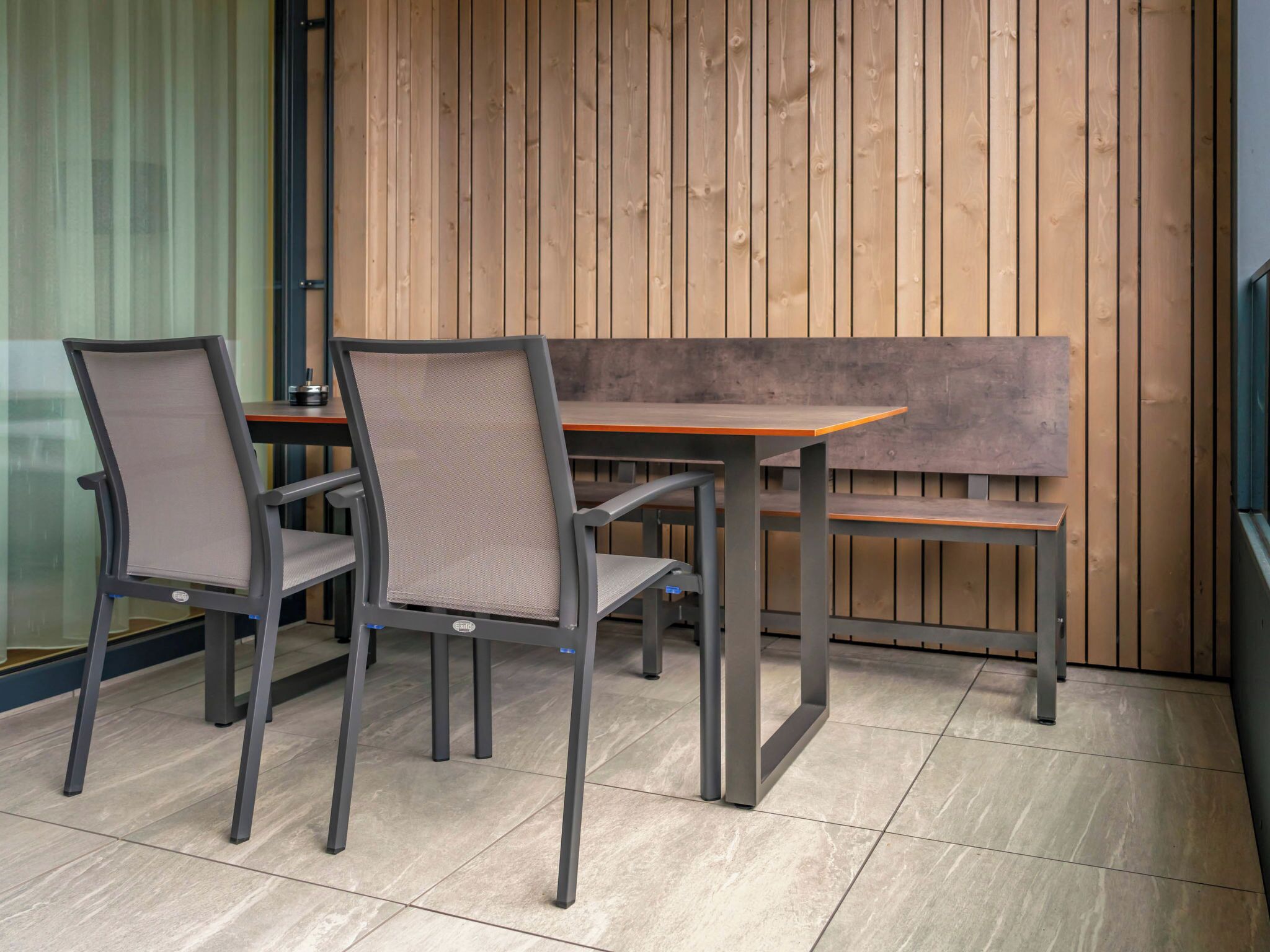 A modern outdoor seating area with a wooden bench and metal chairs.