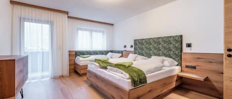 Quarto de hotel moderno com duas camas, cabeceiras de madeira, cômoda de madeira e uma janela grande com cortinas leves.