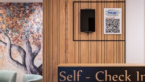 Un espace d’enregistrement autonome avec un mur en panneaux de bois, un code QR et un panneau d’information.