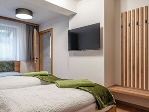 Ett hotellrum med två sängar, en platt-TV, en väggpanel av trä och ett fönster med gardiner.