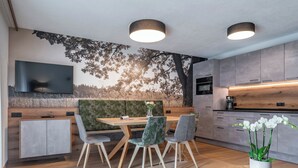 Un espace de restauration moderne avec une table et des chaises en bois, une grande fresque murale et une cuisine aux meubles gris.