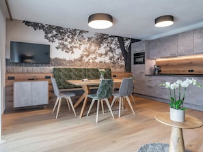 Ein moderner Essbereich mit Holztisch und -stühlen, einer großen Wandmalerei und einer Küche mit grauen Schränken.