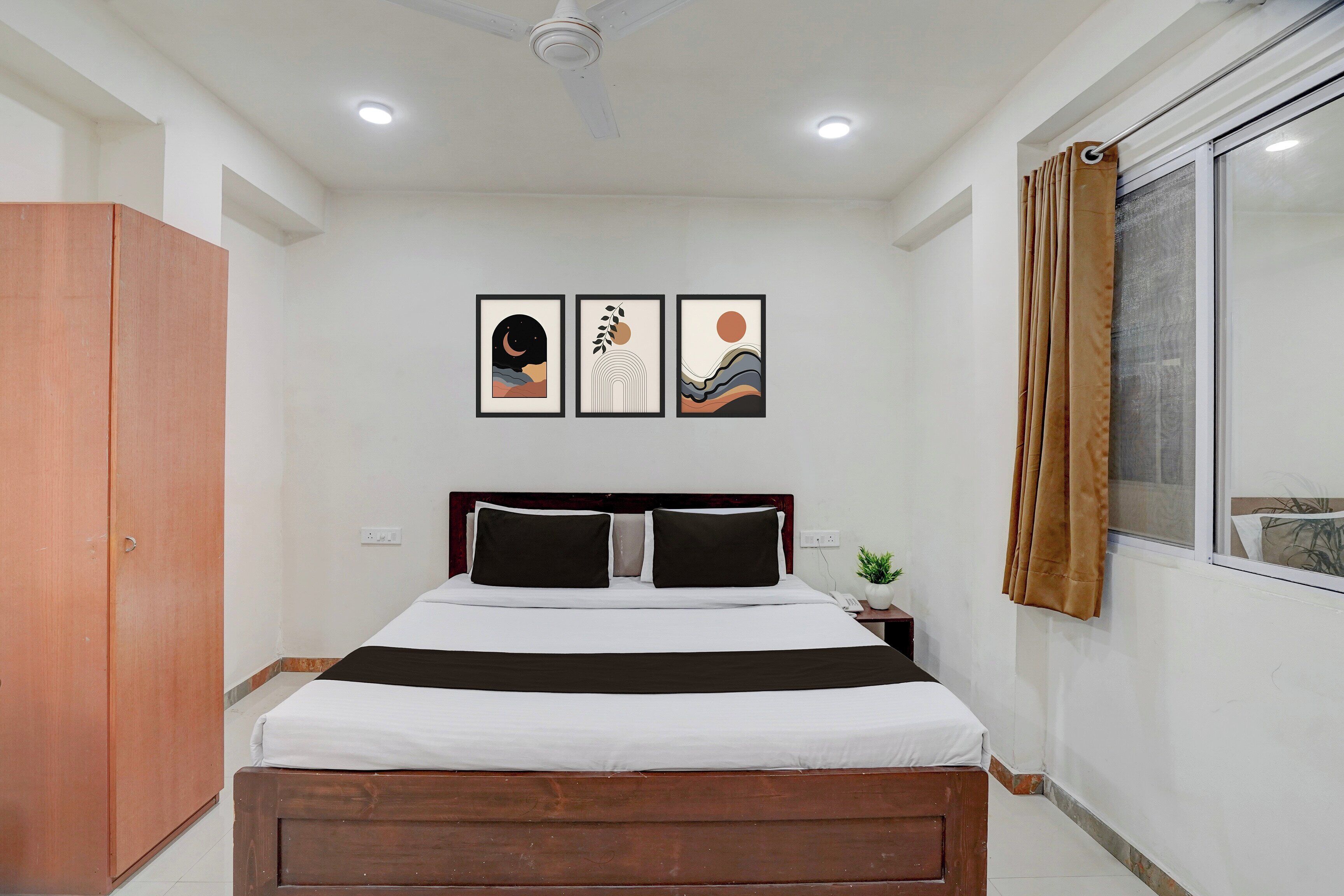 Quarto de hotel com uma cama, um guarda-roupa, uma janela com cortinas e duas molduras na parede.