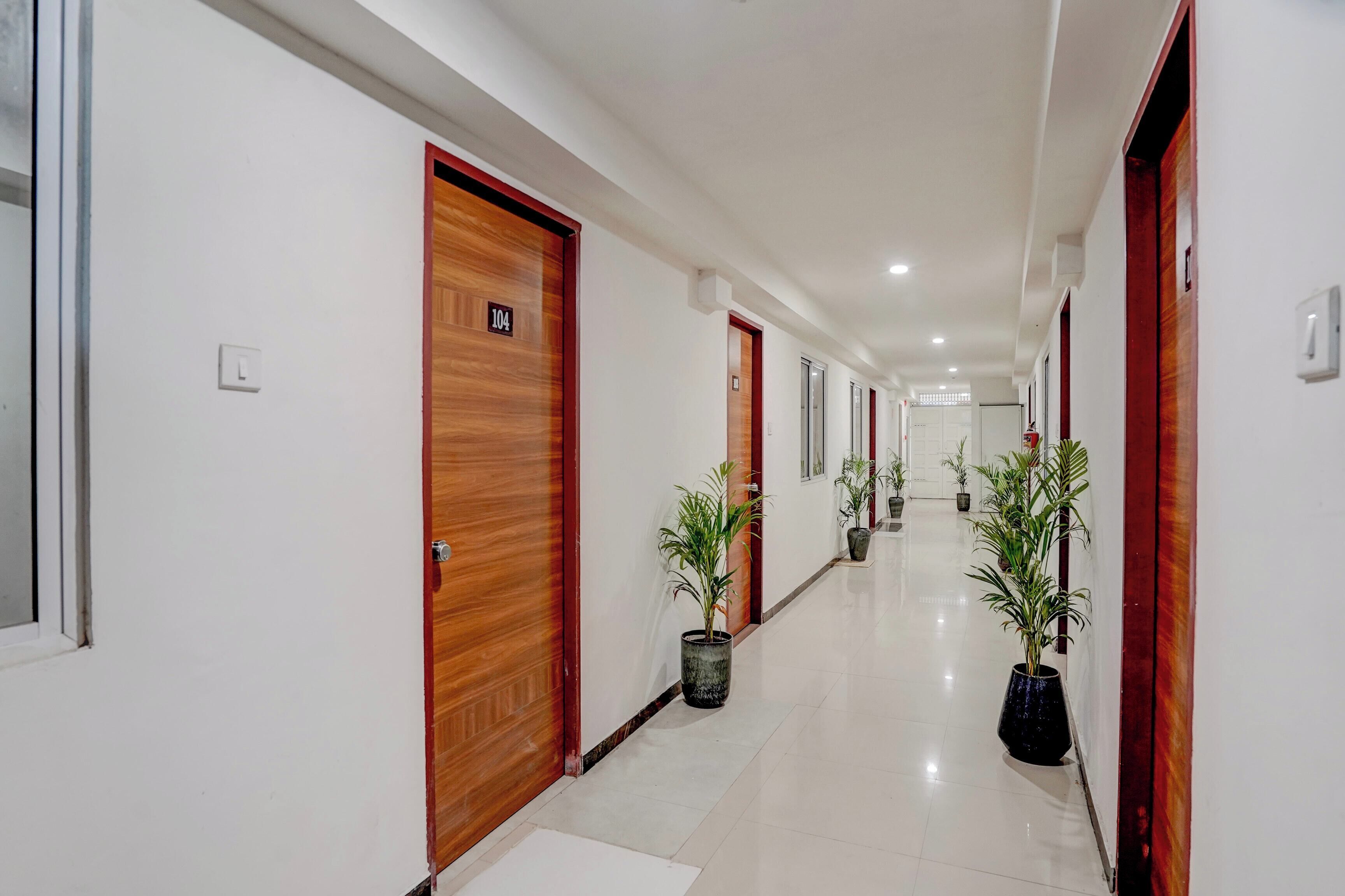 Pasillo de hotel con puertas de madera, letreros de habitaciones numeradas y plantas en macetas.