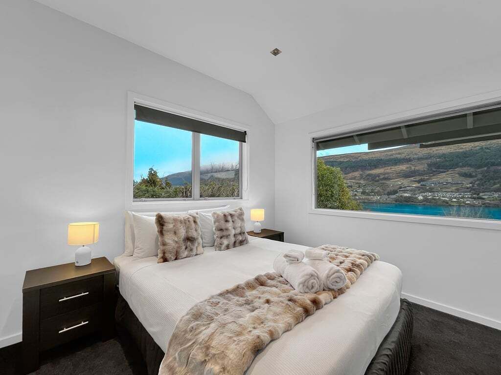 A bedroom with a large bed, two bedside tables, and a view of a landscape through the windows.