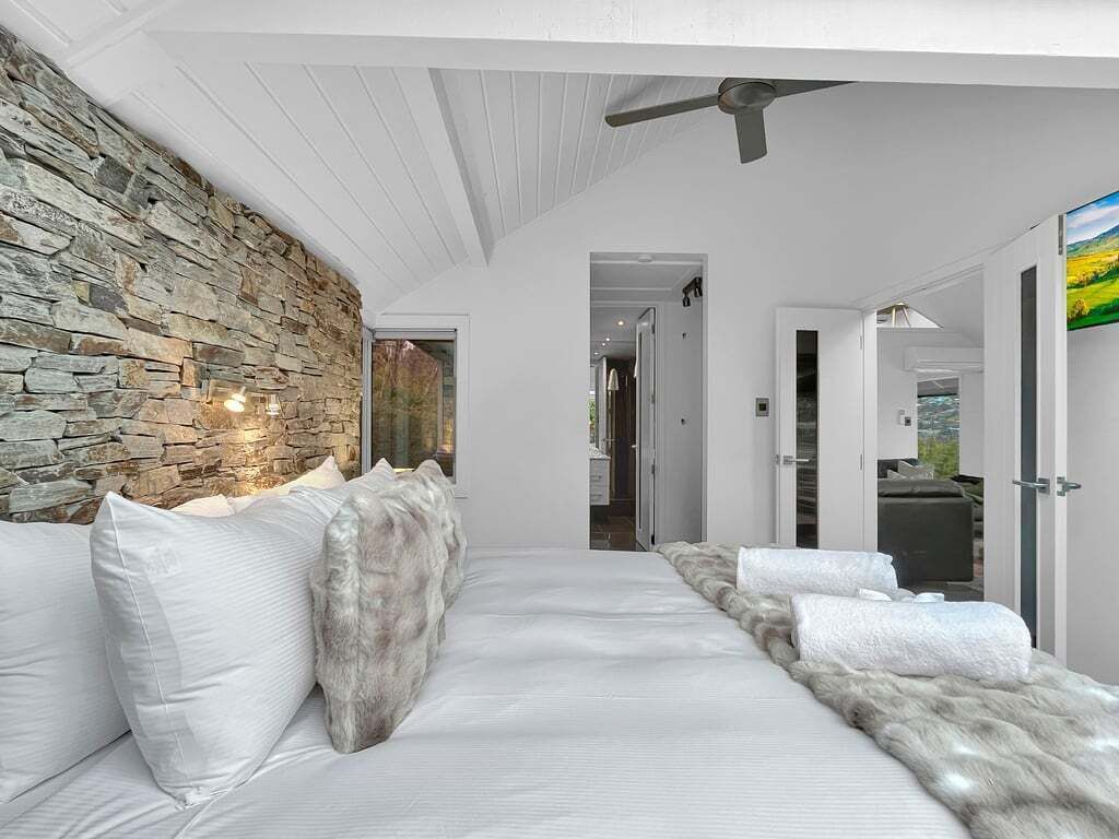 A bedroom with a stone wall, a ceiling fan, and a view of the outdoors.