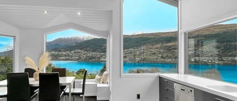 A modern kitchen with large windows, a dining area with a view of a lake and mountains, and a clean, contemporary design.