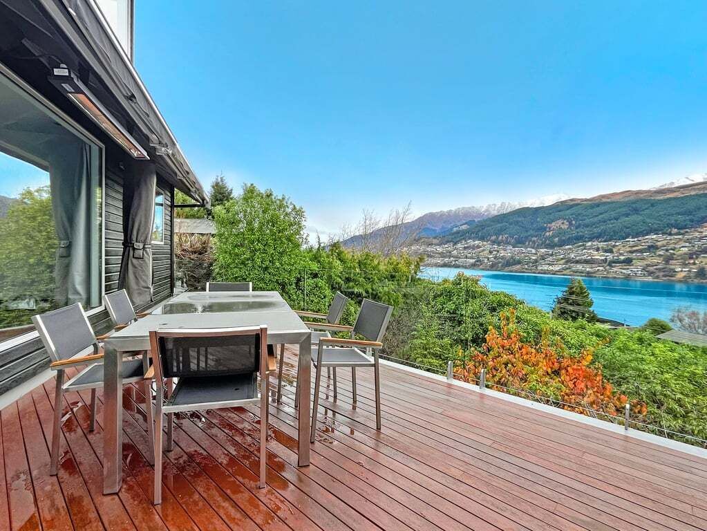 A wooden deck with a table and chairs, overlooking a scenic landscape with mountains and a body of water.