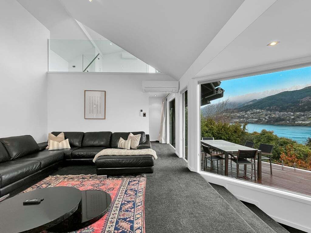 A modern living room with a black leather sofa, a patterned rug, and a view of a coastal landscape.