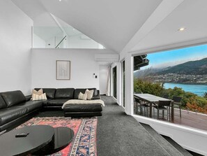 A modern living room with a black leather sofa, a patterned rug, and a view of a coastal landscape.