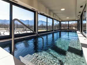 A swimming pool with clear water, a metal ladder, and large windows offering a view of mountains. - Vacation home Alfa by Interhome (Lovinac)