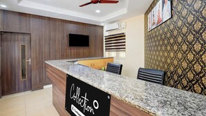 A reception desk with a sign reading 'Collection,' a ceiling fan, a flat-screen TV, and patterned wallpaper.