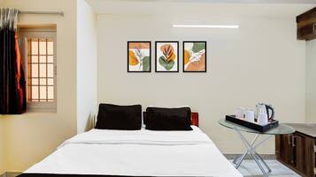 Habitación de hotel con una cama, dos almohadas, una mesita con un hervidor, tazas y una bandeja, y tres cuadros en la pared.