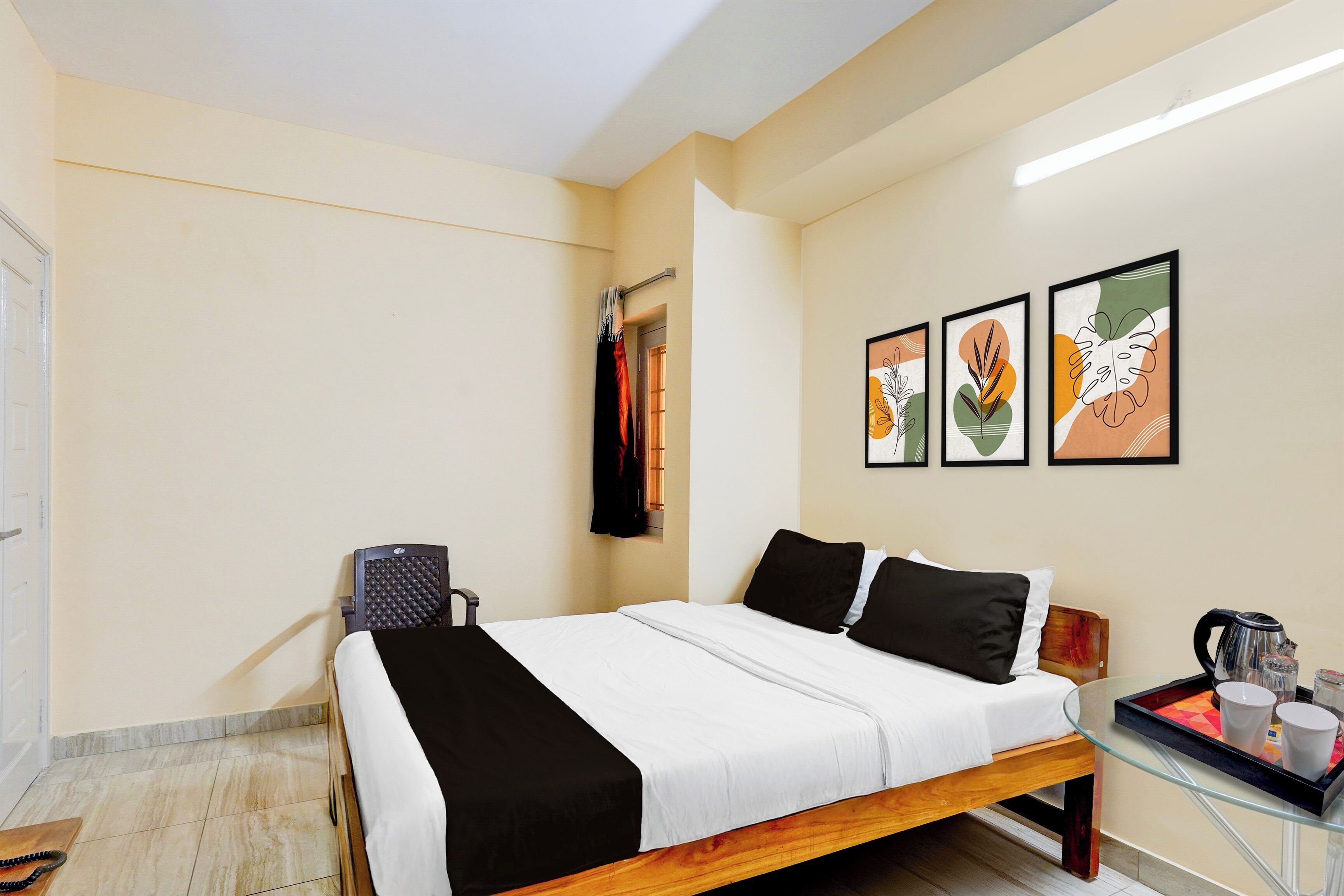Una camera d'albergo con un letto, un comodino con un bollitore e tre opere d'arte incorniciate appese al muro.