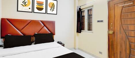 A hotel room with a bed, a wooden door, and three framed artworks on the wall.
