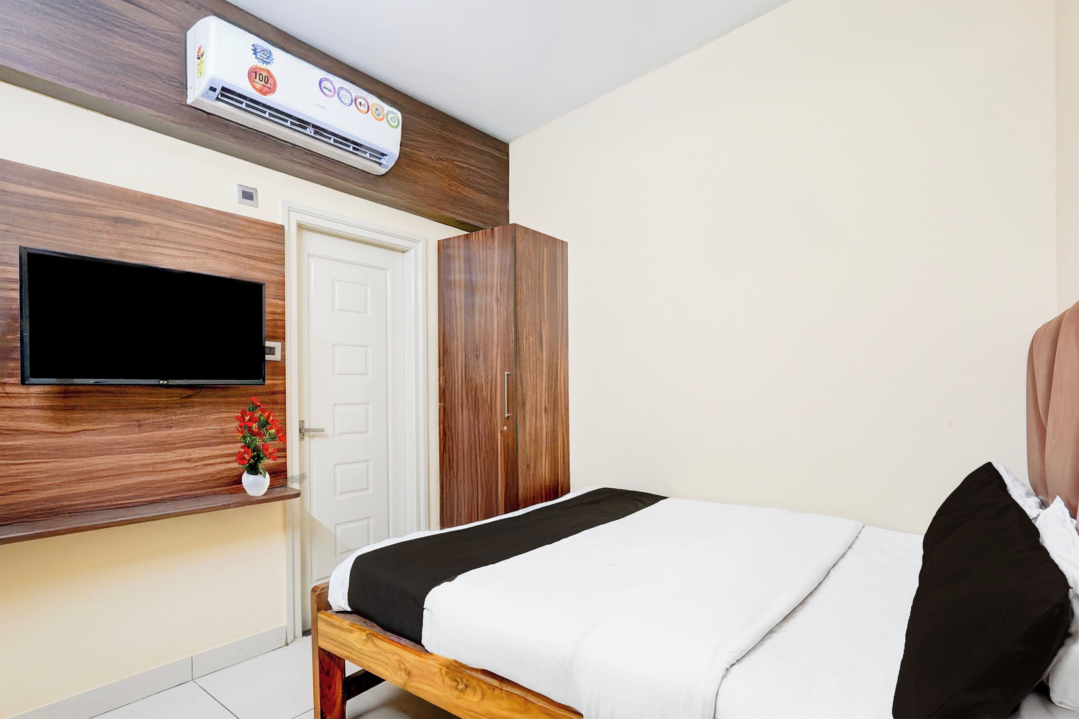 A bedroom with a bed, a TV mounted on the wall, a wardrobe, and an air conditioning unit.