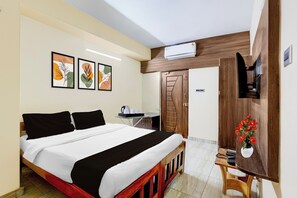A hotel room with a bed, a desk with a kettle, a TV, and a door with a unique design.
