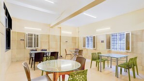 A dining area with a round glass table and chairs, a high ceiling with recessed lighting, and a window with bars.