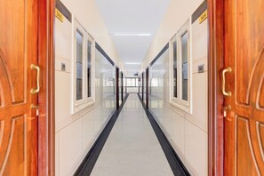 A corridor with doors marked with numbers, a tiled floor, and a ceiling with lights.