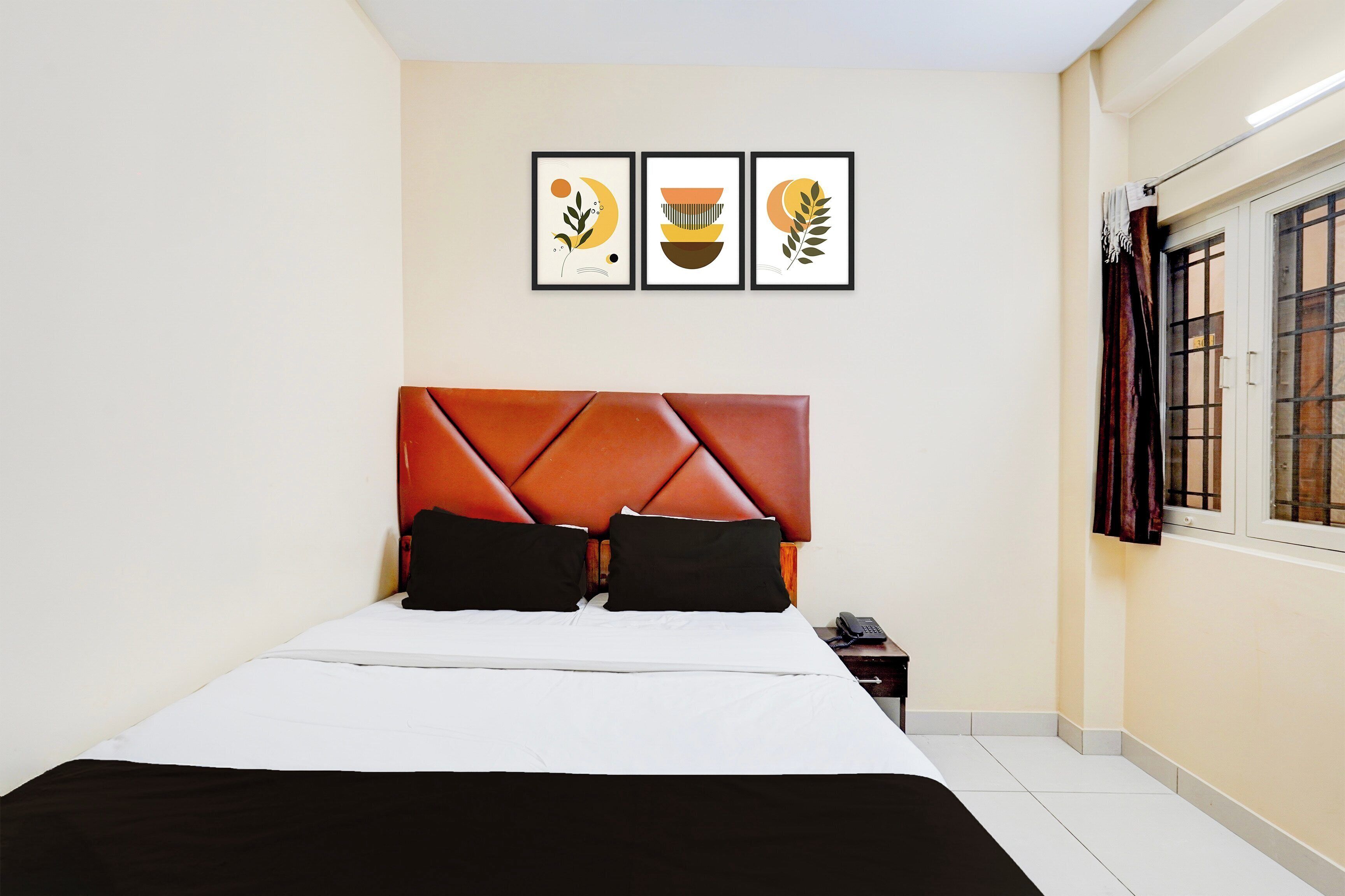 A hotel room with a bed, a nightstand, a telephone, and three framed artworks on the wall.