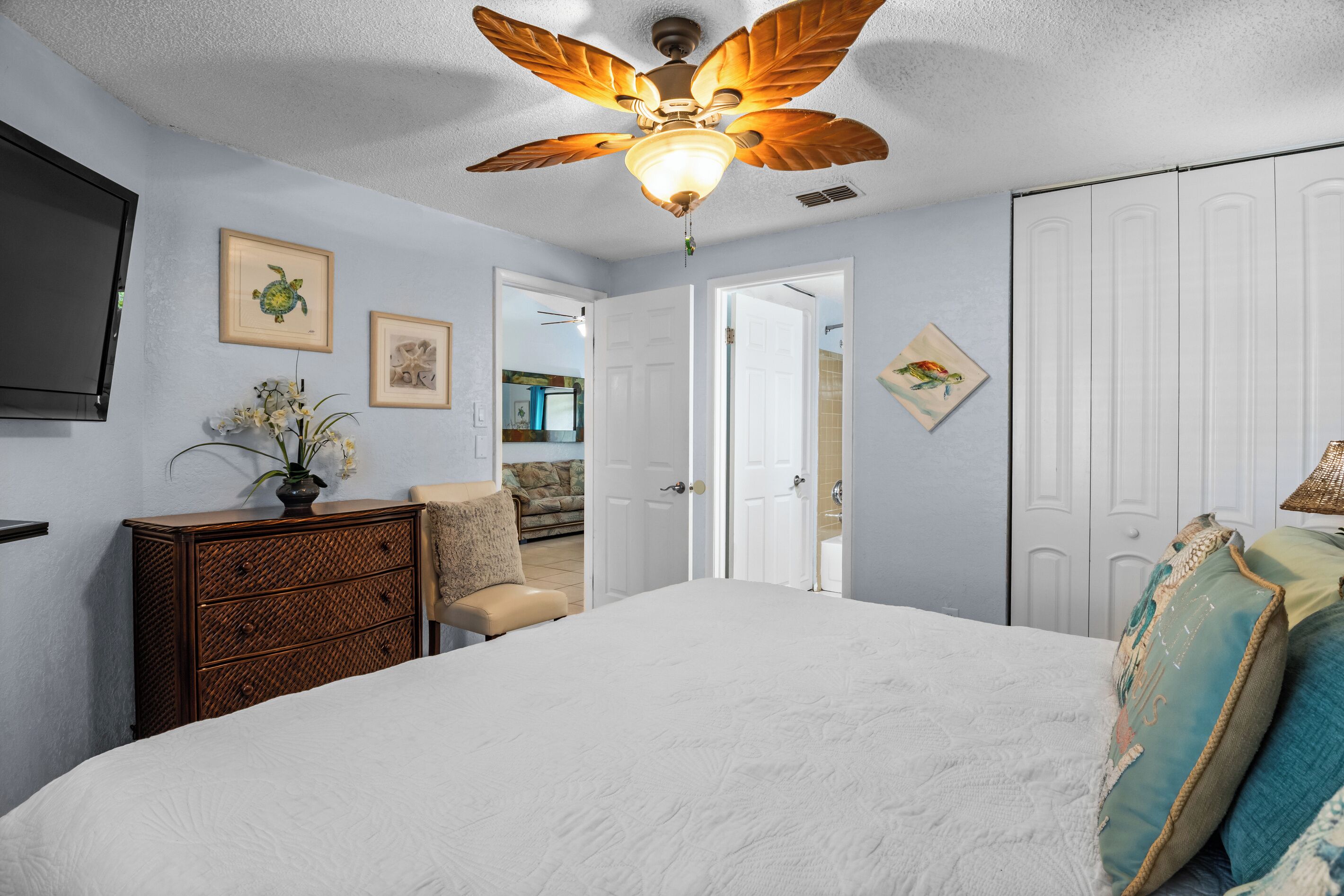 Un dormitorio con ventilador de techo, cama, cómoda y puerta que da a otra habitación.