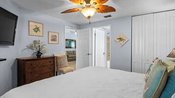 Un dormitorio con ventilador de techo, cama, cómoda y puerta que da a otra habitación.