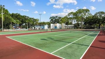 A tennis court with multiple courts, surrounded by trees and a building with a blue roof.