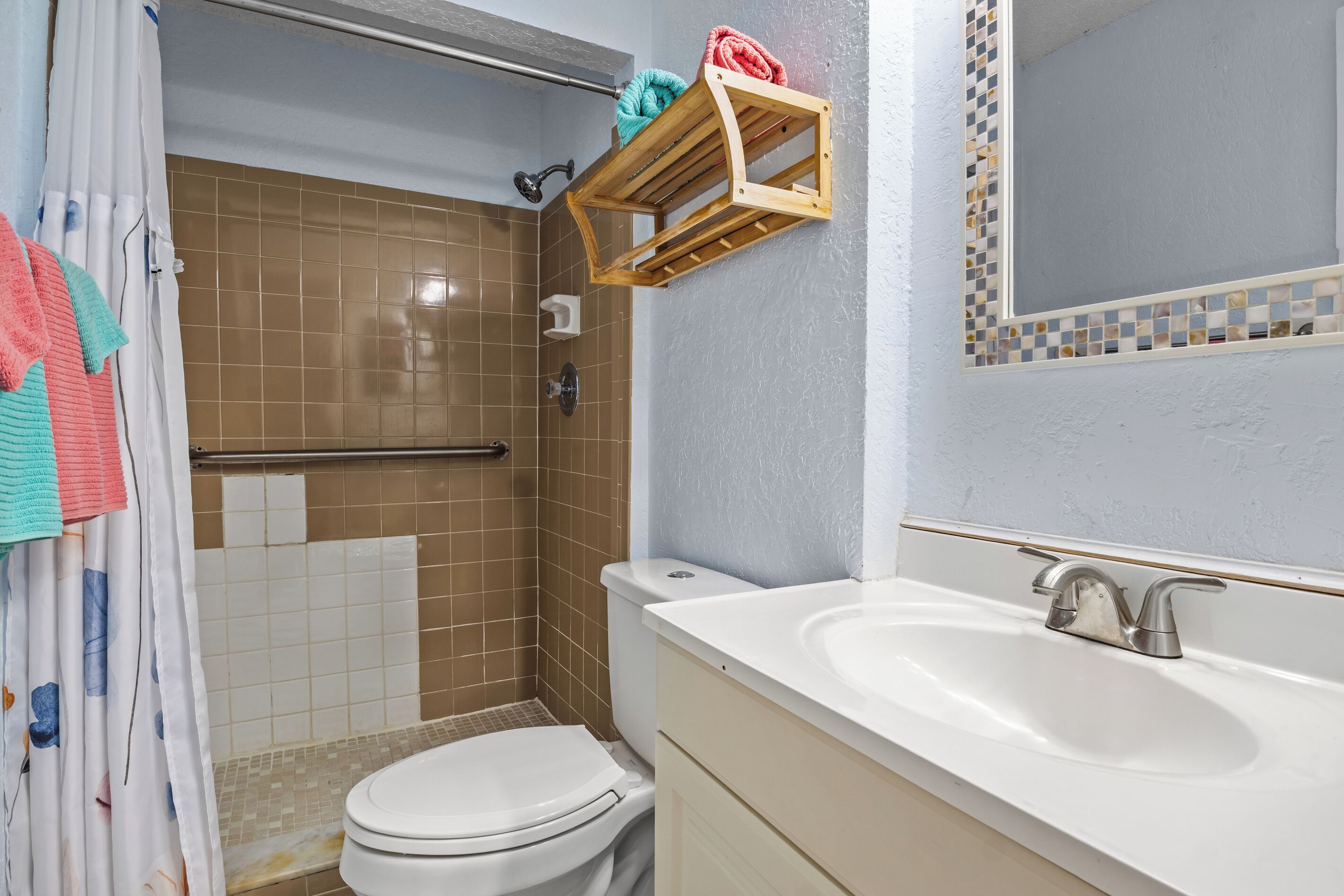 A bathroom with a shower, toilet, sink, and a mirror with a mosaic border.