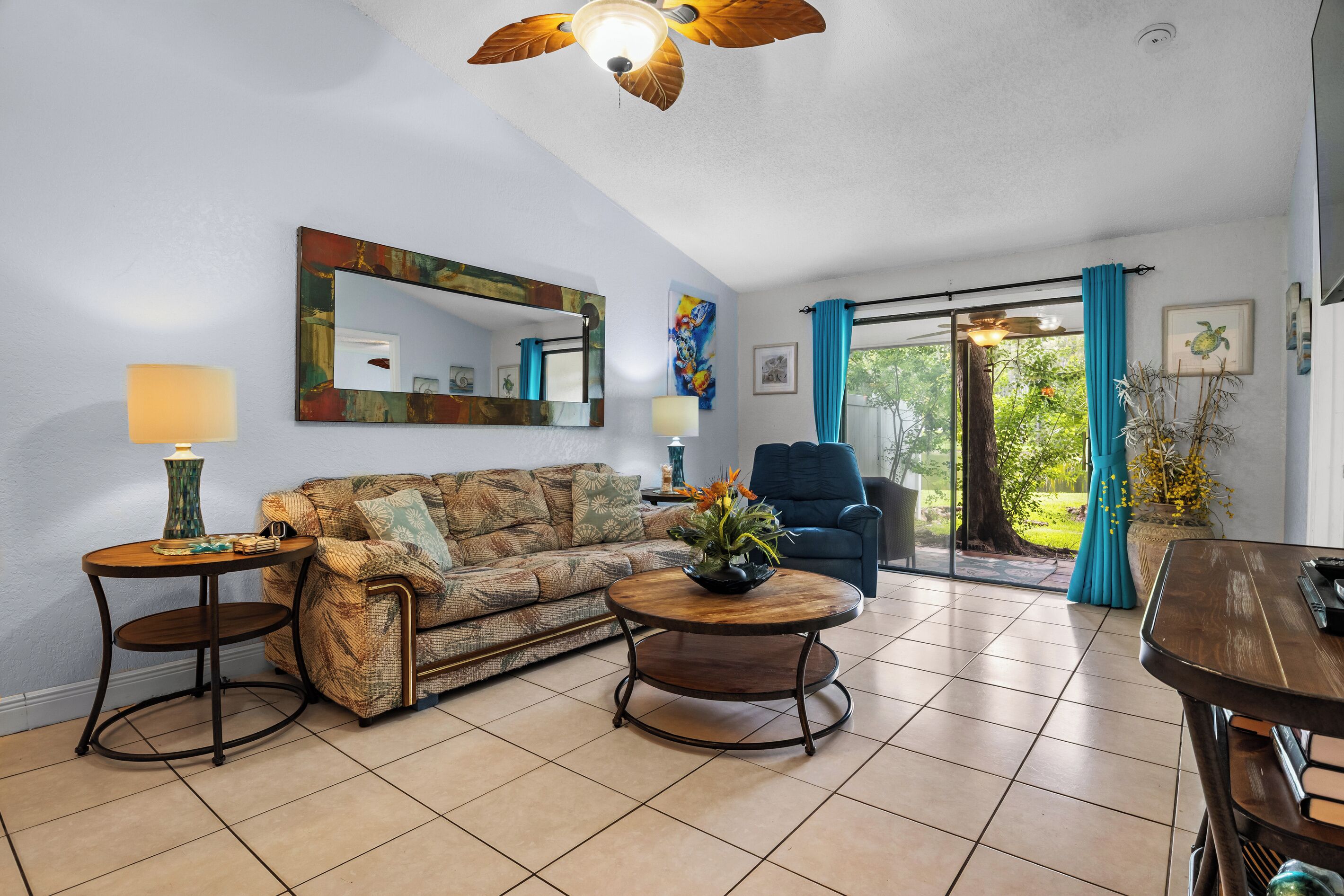 A living room with a sofa, two side tables, a ceiling fan, and a view through a glass door.