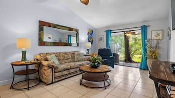 A living room with a sofa, two side tables, a ceiling fan, and a view through a glass door.