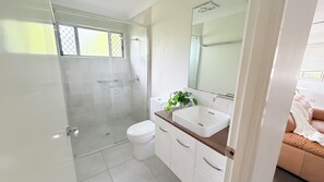 Ein modernes Badezimmer mit einer Duschkabine aus Glas, einer weißen Toilette und einem Waschbecken mit Spiegel darüber.