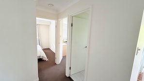 Ein schmaler Flur mit einer Tür zu einem Schlafzimmer mit Bett und Fenster.