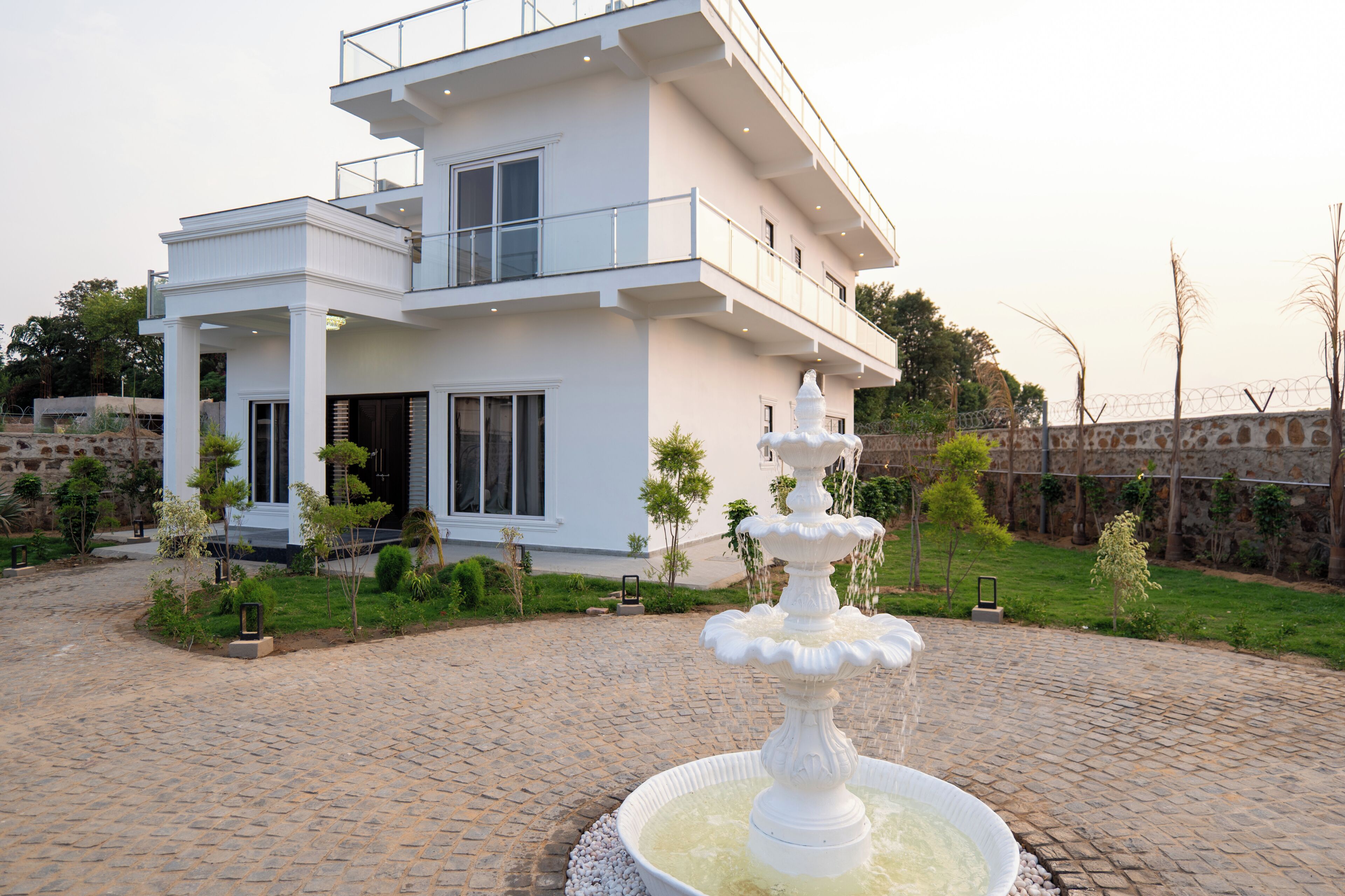 Una casa moderna de dos pisos con fachada blanca, un porche cubierto y una fuente central.