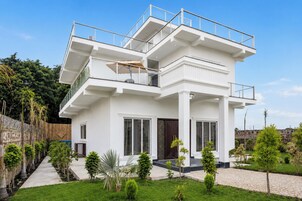 Una casa moderna de dos pisos con un balcón, ventanas amplias y un jardín cuidado.