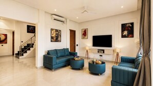 A modern living room with a sofa set, a flat-screen TV, and artwork on the walls. - ELIVAAS JP Farm Stay 5BHK Villa With Bar (Baghanki)