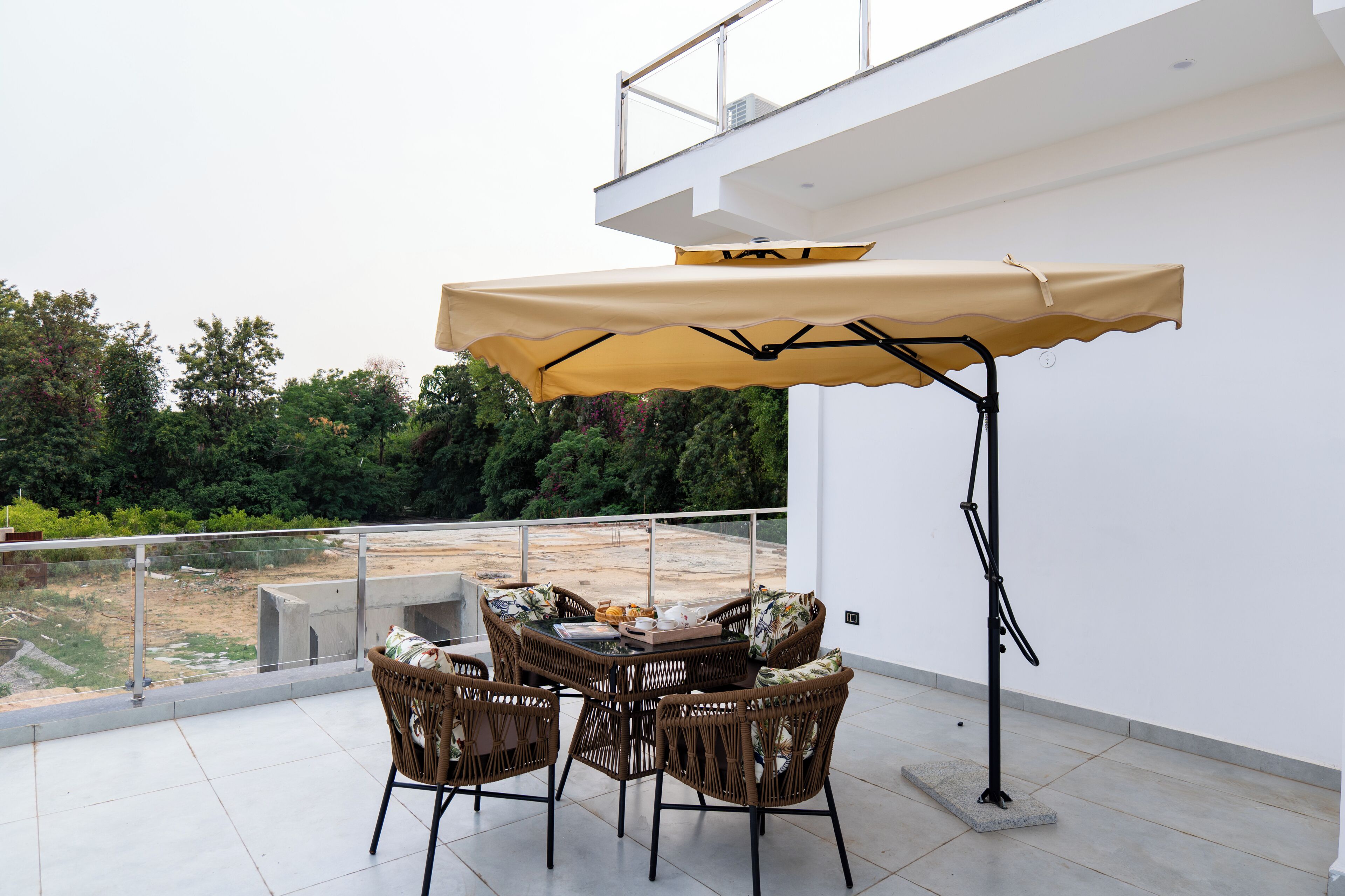 Ein Balkon mit Korbstühlen, einem Tisch und einem beige farbenen Sonnenschirm.