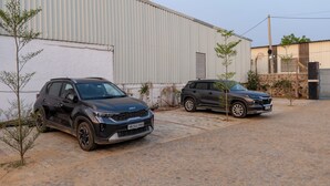 Two parked SUVs in front of a building with corrugated metal siding and a paved ground. - ELIVAAS JP Farm Stay 5BHK Villa With Bar (Baghanki)