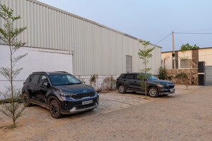 Two parked SUVs in front of a building with corrugated metal siding and a paved ground.