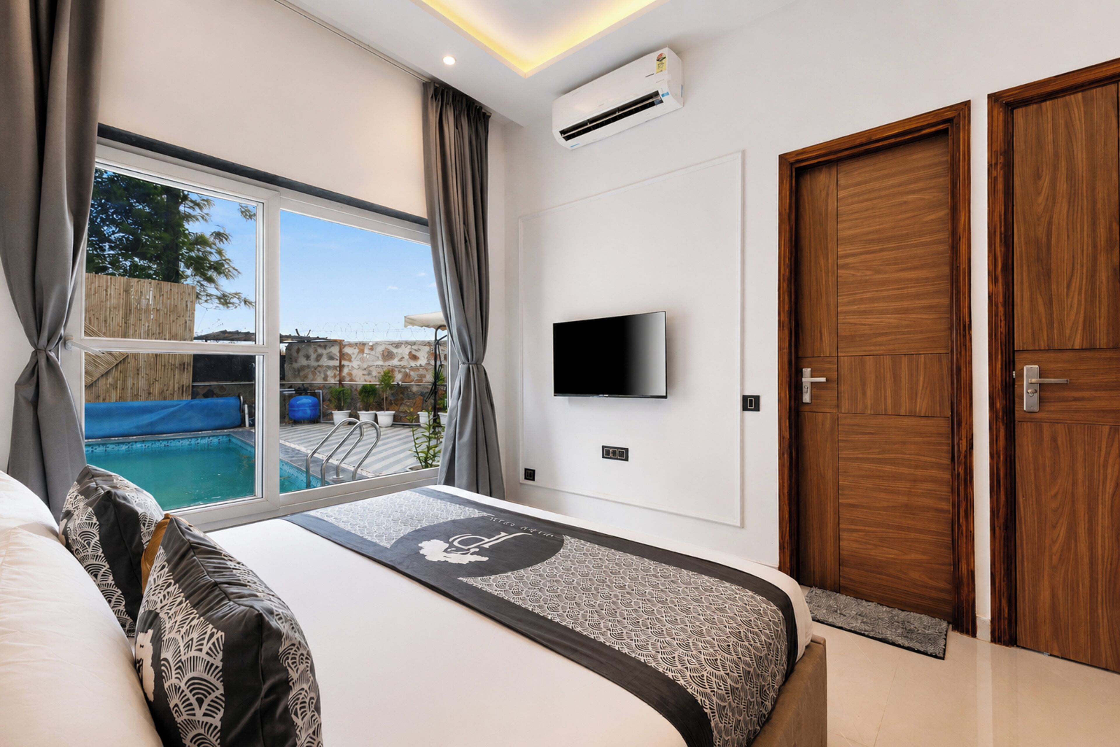 A modern hotel room with a large bed, a TV mounted on the wall, and a view of a swimming pool.