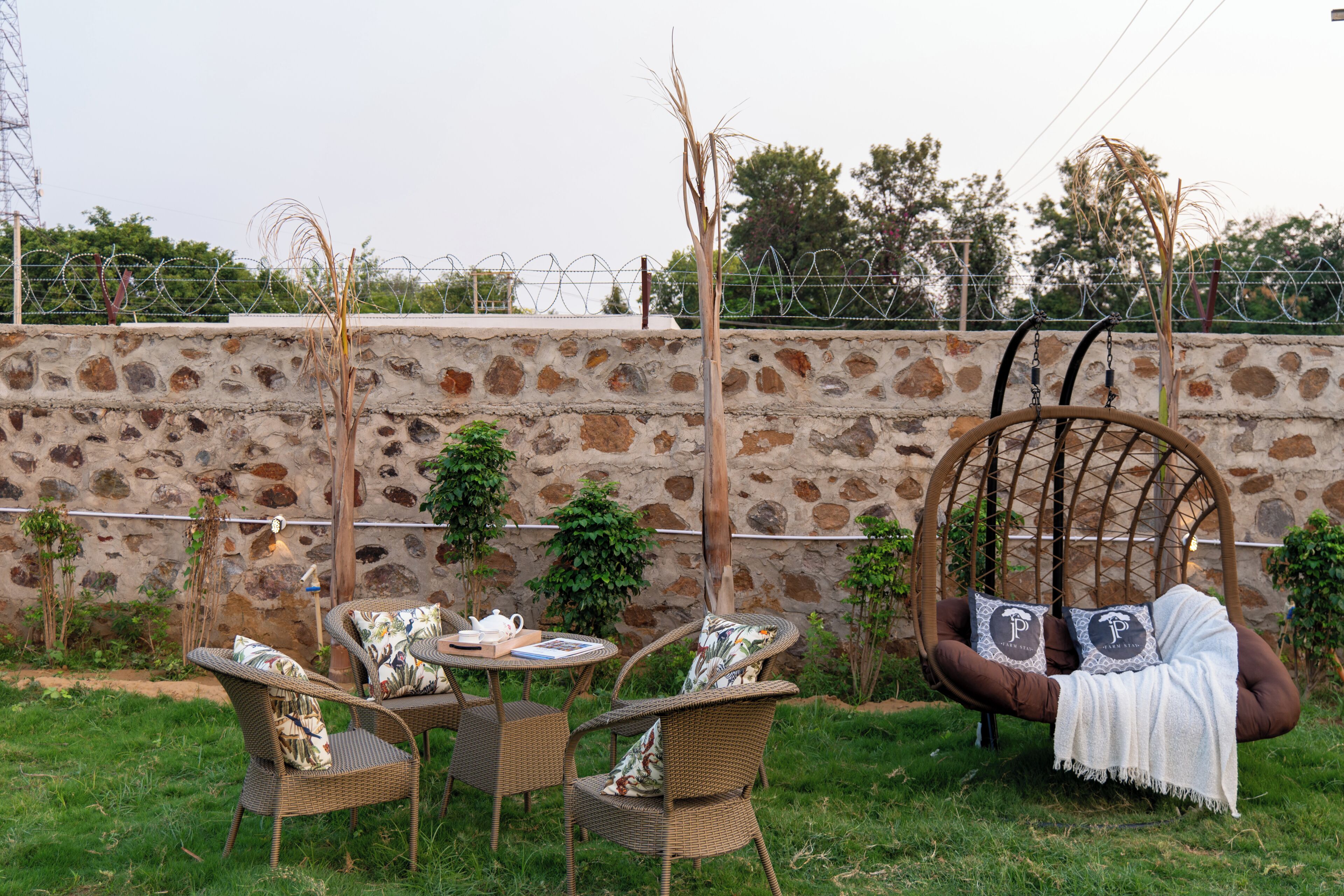 Un jardín con mobiliario de mimbre, una silla colgante y un muro de piedra.