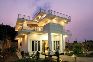 A modern two-story house with a balcony, large windows, and a well-lit entrance.