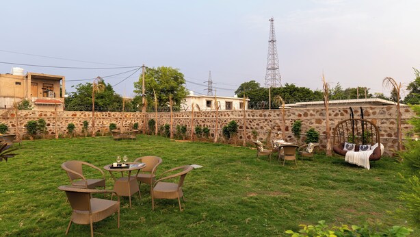 A grassy outdoor area with wicker furniture, a swing, and a stone wall. - ELIVAAS JP Farm Stay 5BHK Villa With Bar (Baghanki)